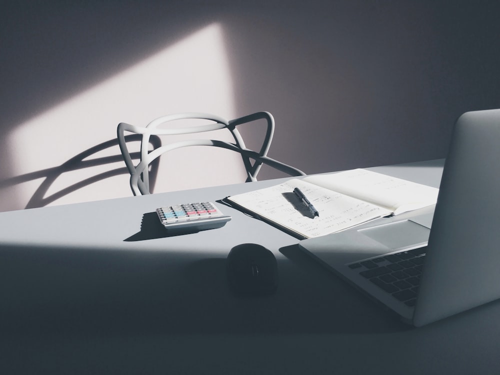 A modern white chair at a table with a laptop, a notebook and a calculator